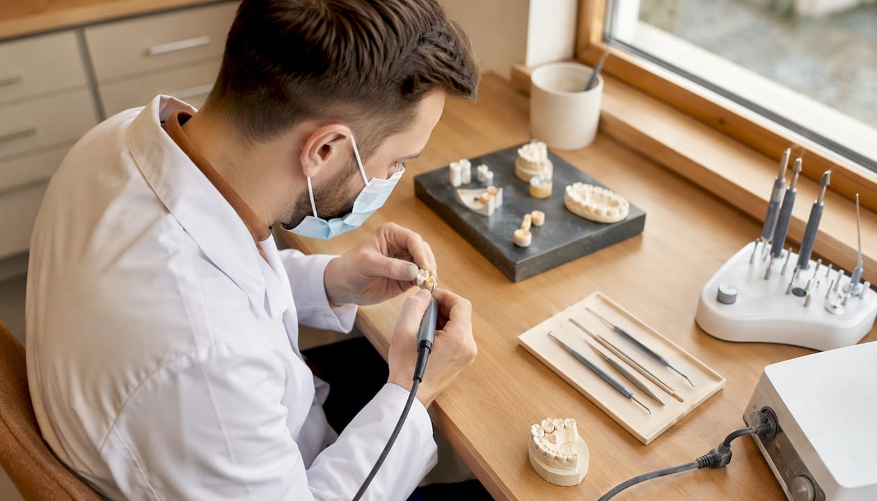 Tehnicianul dentar finisează cu atenție o coroană ceramică pentru a-i oferi un aspect cât mai natural și estetic.